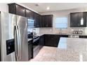 Modern kitchen with stainless steel appliances, dark cabinets, granite countertops, and tiled backsplash at 398 Citrus Isle Loop, Davenport, FL 33837