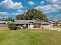 Charming single-story home with a lush green lawn, stone accents, and mature trees under a bright, cloudy sky at 9501 Holbrook Dr, Orlando, FL 32817
