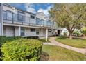 Two-story condo with sidewalk and blue railings, complemented by lush landscaping and a large shade tree at 2568 Woodgate Blvd # 204, Orlando, FL 32822