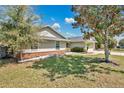 Side view of a cozy home featuring a brick foundation, lush lawn, and mature trees at 8703 Grandee Dr, Orlando, FL 32829