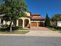 Charming two-story home featuring a red tile roof, arched entryway, a three-car garage, and lush landscaping at 15149 Canoe Pl, Winter Garden, FL 34787