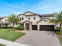 Inviting two-story home featuring a manicured lawn, palm trees, and a paver driveway leading to a two-car garage at 676 Bishop Bay Loop, Apopka, FL 32712