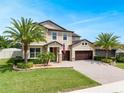 Inviting two-story home featuring a manicured lawn, palm trees, and a paver driveway leading to a two-car garage at 676 Bishop Bay Loop, Apopka, FL 32712