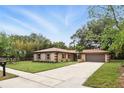 Single-story home with a well-maintained lawn, mature trees, and an attached two-car garage on a sunny day at 100 Des Pinar Ln, Longwood, FL 32750