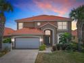 Charming two-story home featuring a red tile roof, arched entryway, and a well-manicured lawn with mature palm trees at 330 Rosso Dr, Davenport, FL 33837