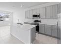 Well-lit kitchen with stainless steel appliances, gray cabinets, a spacious island, and tiled floors at 2030 Firethorn Loop, Haines City, FL 33844