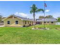 Inviting single-story yellow home with a well-manicured lawn, palm tree, and an American flag at 5800 Spruce Creek Woods Dr, Port Orange, FL 32127