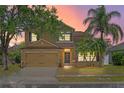 Inviting two-story home with a manicured lawn, mature trees, and warm exterior lighting at sunset at 108 Portstewart Dr, Orlando, FL 32828