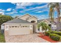 Beautiful front yard with brick pavers, lush bushes, and a two car garage under a blue cloudy sky at 10621 Golden Cypress Ct, Orlando, FL 32836