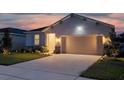 Single-story home's front exterior at dusk, featuring a two-car garage and illuminated landscaping at 2731 Rowan St, Tavares, FL 32778