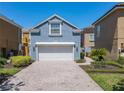 Charming light blue home with a white garage door, and brick-paved driveway lined with lush landscaping at 7409 Excitement Dr, Reunion, FL 34747