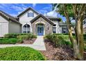 Charming home featuring a stone entrance, blue door, lush landscaping and manicured lawn at 25519 Hawks Run Ln, Sorrento, FL 32776