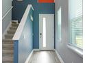 Modern entryway with sleek white door, gray wood floors, blue walls, and staircase at 1628 Little Wren Ln, Winter Park, FL 32792