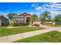 Charming single-story home featuring a well-manicured lawn, tropical landscaping, and brick accents under a blue sky at 4027 Sunrise Ridge Blvd, Groveland, FL 34736
