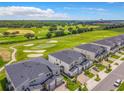 Aerial view of modern townhomes adjacent to a lush green golf course under a bright blue, partly cloudy sky at 507 Ocean Course Ave # 507, Davenport, FL 33896