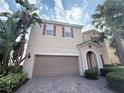 Beige two-story home featuring a two-car garage, red shutters, and tropical landscaping at 11962 Autumn Fern Ln, Orlando, FL 32827