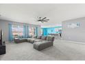Spacious living room with large windows, comfortable gray sectional sofa, ceiling fan, and views into the kitchen at 445 Auburn Grove Pl, Auburndale, FL 33823