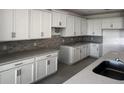 Modern kitchen featuring white cabinets, gray backsplash, sleek countertops, and stainless steel sink at 7138 Rolling Leaf Rd, Groveland, FL 34736