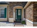 Close-up of front door with green paint, decorative glass, and stacked stone surround at 13247 Hatherton Cir, Orlando, FL 32832