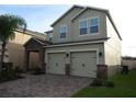 Two-story home with a brick driveway, two-car garage, stone details, and muted green paint at 2737 Monticello Way, Kissimmee, FL 34741