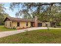 Single-story home exterior featuring stucco siding, brick chimney, mature trees, and two car garage at 4495 Bedford Rd, Sanford, FL 32773