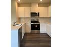 Modern kitchen featuring white cabinets, stainless steel appliances, quartz countertops, and sleek dark wood-look flooring at 989 Commons Way, Port Orange, FL 32129