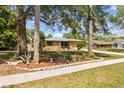 Landscaped brick home with a green roof surrounded by lush greenery and blooming flowers at 255 Katrina St, De Leon Springs, FL 32130