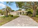 Elegant single-story home featuring a curved driveway, manicured lawn, and a mature shade tree at 1320 Antrim Cir, Ormond Beach, FL 32174