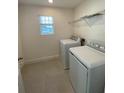 Well-lit laundry room equipped with a washer, dryer, shelving and tiled floor, offering convenience and efficiency at 14746 Erice Ave, Clermont, FL 34714