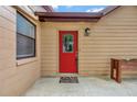 Close-up of the decorative front door of this tan home showing a red door with glass insert and decorative welcome mat at 150 Debary Dr, Debary, FL 32713