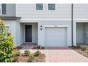 Close-up of a townhouse with a brick paver driveway, gray door and garage door, and manicured bushes at 16434 Bird Of Paradise Ave, Clermont, FL 34714