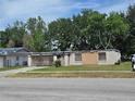 Exterior side view of the home featuring boarded-up windows and overgrown landscaping at 2467 Myakka Dr, Orlando, FL 32839