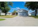 Single-story home with an attached garage and landscaped front yard with trees under a bright blue sky at 2709 Prestwick Ln, Kissimmee, FL 34744
