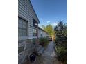 A home's side yard featuring a stone foundation, window, utility hookups and a walkway toward the backyard at 7506 Mott Ave, Orlando, FL 32810