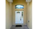 Inviting front entrance with a white door, arched transom window, and neutral stucco walls at 6730 Orlando Drive, Indian Lake Estates, FL 33855