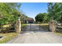 View of a house and yard beyond the stone and wood entry posts and a black metal driveway gate at 21343 Reindeer Rd, Christmas, FL 32709