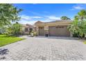 Paver driveway leads to a well-maintained home with a two-car garage and tropical landscaping at 196 Torino Ln, Kissimmee, FL 34759