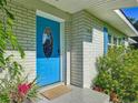 Close up of the home's bright blue front door with oval window, grey brick, and colorful, manicured landscaping at 1118 Ne 17Th Ave, Ocala, FL 34470