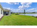 Expansive backyard with lush green grass leading to a serene lake, with a screened-in lanai at 6121 Blue Pond Way, St Cloud, FL 34771
