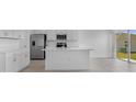 Bright open-concept kitchen with stainless steel appliances, white cabinets, a kitchen island, and sliding doors to the backyard at 5109 Forget Me Not Ave, Lake Hamilton, FL 33851