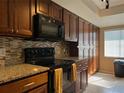 Kitchen with granite counters, tile backsplash, and dark wood cabinets with black appliances at 909 Royalton Rd, Orlando, FL 32825