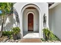 Grand arched entryway with a wooden door flanked by lantern-style sconces and potted ferns at 9743 Covent Garden Dr, Orlando, FL 32827