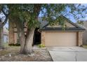 Two story tan house with a two-car garage, with a large tree in the front yard at 2239 Meadowmouse St, Orlando, FL 32837