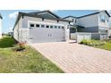 A wide gray two-car garage is featured with stone accents and a brick driveway at 667 Pennywort St, Lake Alfred, FL 33850