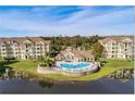 Aerial view of condo buildings surrounding a pool and clubhouse, with a serene lake in the foreground at 5276 Cane Island Loop # 302, Kissimmee, FL 34746