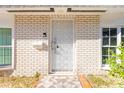 Close-up of the front door featuring a white security door and brick facade, accented by decorative plants and natural light at 315 Glenview Blvd # 3, Daytona Beach, FL 32118