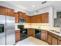 Well-lit kitchen featuring wooden cabinetry, stainless steel refrigerator, and black appliances against light tile flooring at 6636 S Goldenrod Rd # 116B, Orlando, FL 32822
