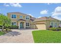 Welcoming exterior of a tan two-story home with a well-kept lawn and a brick-paved driveway leading to a three-car garage at 14545 Braddock Oak Dr, Orlando, FL 32837