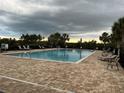 Community pool with brick patio, lounge chairs, and mature trees against a cloudy sky at 176 Jensen Dr, Groveland, FL 34736