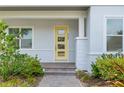 A welcoming, light-filled entrance with a bright yellow front door with modern glass panels and a brick walkway at 7789 Nemours Pkwy, Orlando, FL 32827